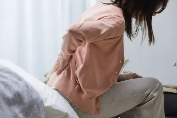 Mulher sentada segurando a lombar com as duas mãos, demonstrando dor nas costas